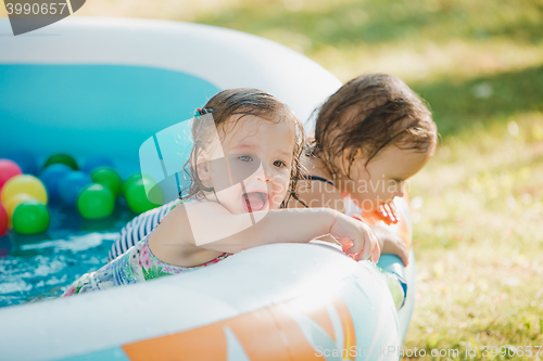 Image of The two little baby girls playing with toys in inflatable pool in the summer sunny day