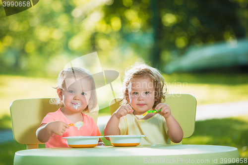 Image of Two little girls sitting at a table and eating together against green lawn