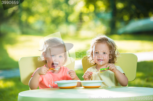 Image of Two little girls sitting at a table and eating together against green lawn