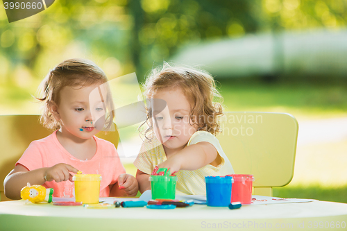 Image of Two-year old girls painting with poster paintings together against green lawn