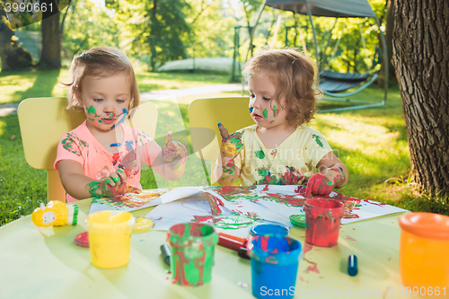 Image of Two-year old girls painting with poster paintings together against green lawn