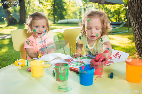 Image of Two-year old girls painting with poster paintings together against green lawn