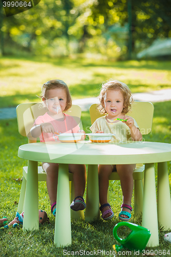 Image of Two little girls sitting at a table and eating together against green lawn