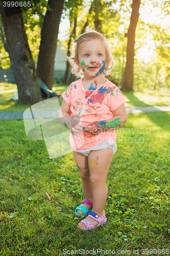 Image of Two-year old girl stained in colors against green lawn