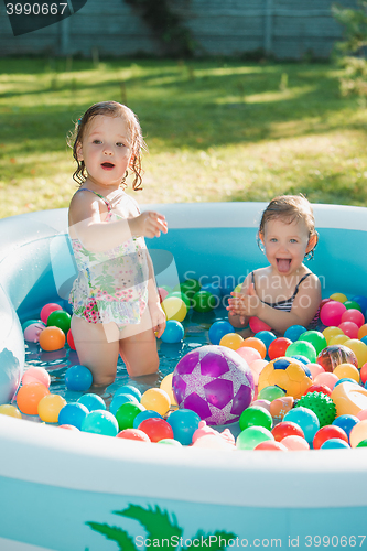 Image of The two little baby girls playing with toys in inflatable pool in the summer sunny day