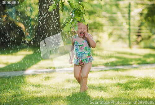 Image of The little baby girl playing with garden sprinkler.