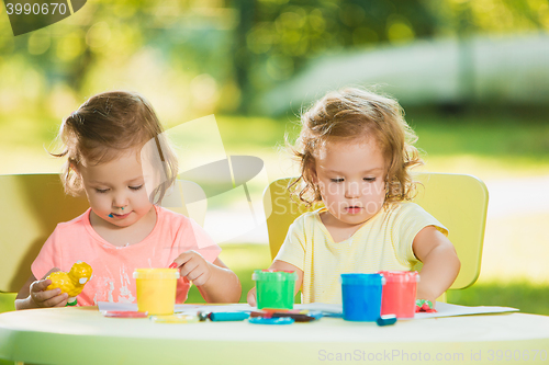 Image of Two-year old girls painting with poster paintings together against green lawn