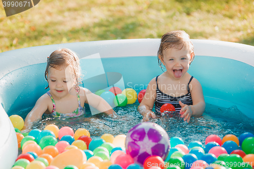 Image of The two little baby girls playing with toys in inflatable pool in the summer sunny day