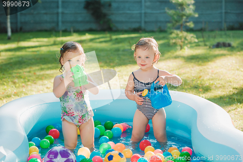 Image of The two little baby girls playing with toys in inflatable pool in the summer sunny day