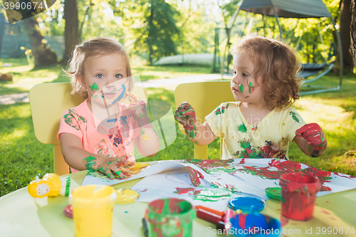 Image of Two-year old girls painting with poster paintings together against green lawn