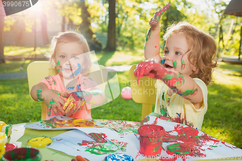 Image of Two-year old girls painting with poster paintings together against green lawn