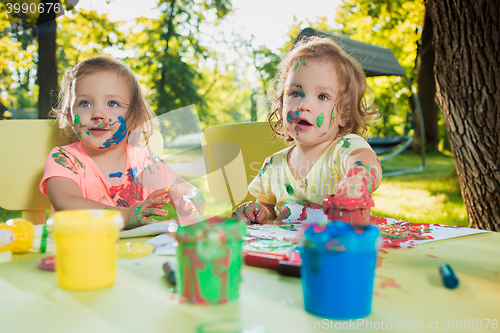 Image of Two-year old girls painting with poster paintings together against green lawn