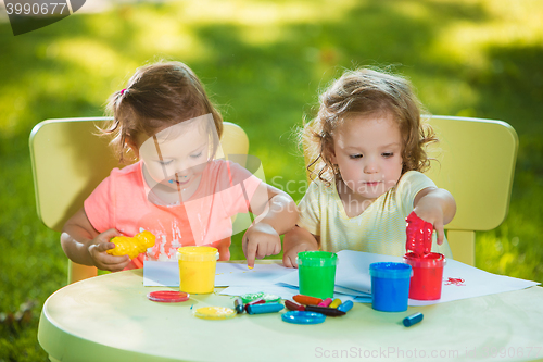 Image of Two-year old girls painting with poster paintings together against green lawn