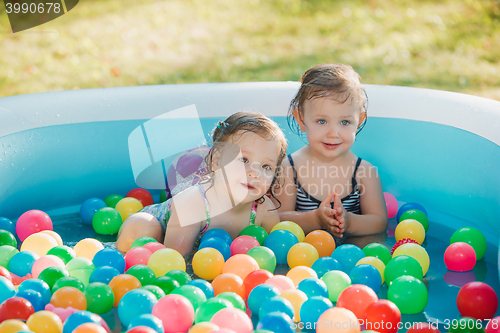 Image of The two little baby girls playing with toys in inflatable pool in the summer sunny day