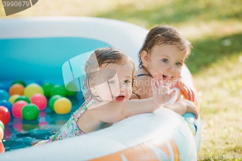 Image of The two little baby girls playing with toys in inflatable pool in the summer sunny day