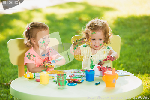 Image of Two-year old girls painting with poster paintings together against green lawn