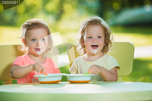 Image of Two little girls sitting at a table and eating together against green lawn