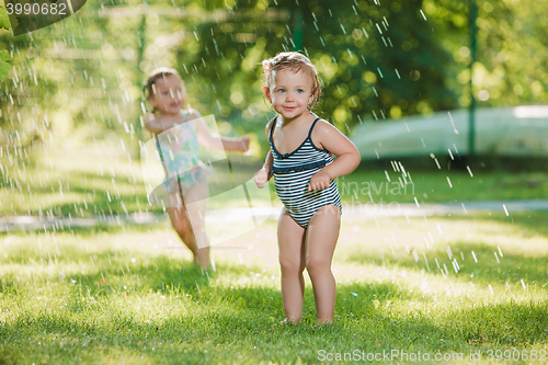 Image of The two little baby girls playing with garden sprinkler.