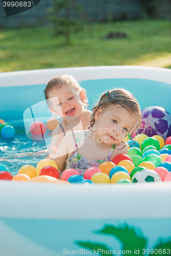 Image of The two little baby girls playing with toys in inflatable pool in the summer sunny day