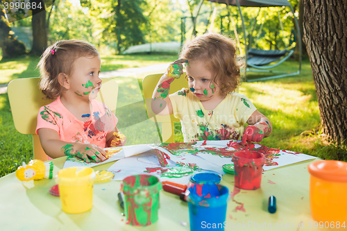 Image of Two-year old girls painting with poster paintings together against green lawn