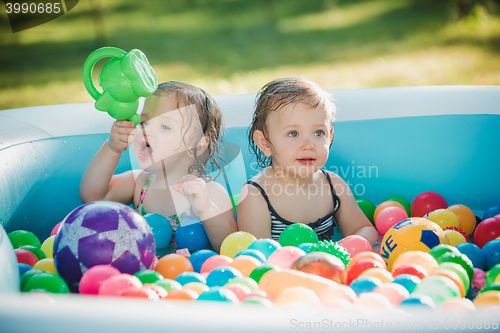 Image of The two little baby girls playing with toys in inflatable pool in the summer sunny day