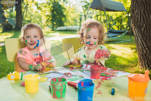 Image of Two-year old girls painting with poster paintings together against green lawn