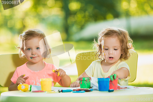 Image of Two-year old girls painting with poster paintings together against green lawn