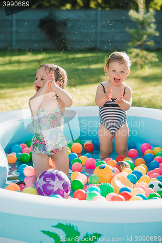 Image of The two little baby girls playing with toys in inflatable pool in the summer sunny day