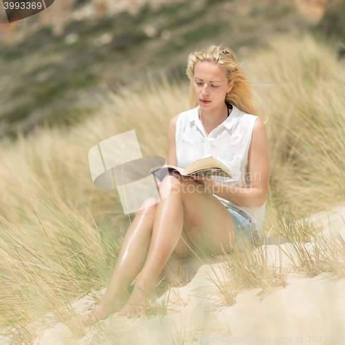 Image of Woman reading book, enjoying sun on beach.