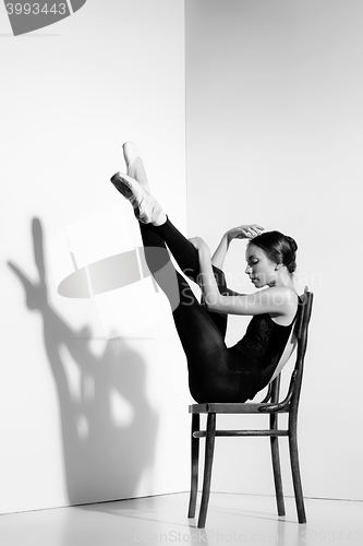 Image of Ballerina in black outfit posing on a wooden chair, studio background.