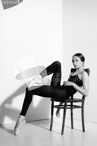 Image of Ballerina in black outfit posing on a wooden chair, studio background.