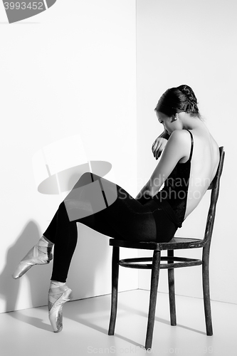 Image of Ballerina in black outfit posing on a wooden chair, studio background.