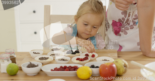 Image of Little girl placing berries on muffins