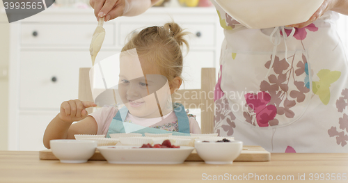 Image of Laughing girl with muffin cups and parent in apron
