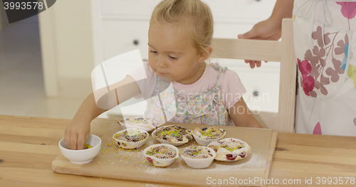 Image of Close up on girl sprinkling toppings  muffins