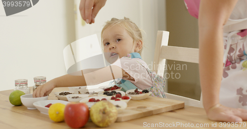 Image of Child watching woman sprinkle candy on muffins