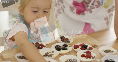 Image of Cute little girl putting berries on muffins