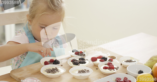 Image of Girl putting berries on muffins  table