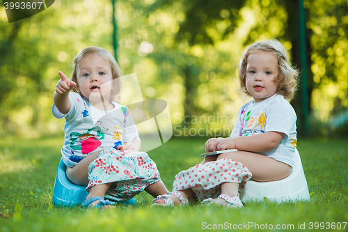 Image of The two little baby girls sitting on pottys against green grass