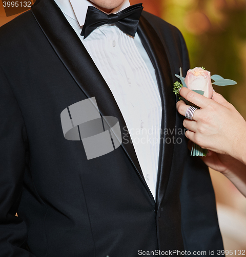 Image of Bride arranging boutonniere flower on suit jacke groom