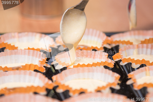 Image of The dough for cakes dripping from a spoon into molds