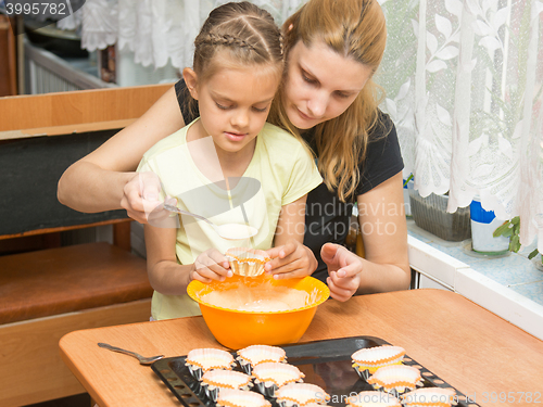 Image of Mom and daughter seven years pour the batter into the mold for baking muffins