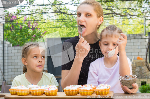 Image of Mother and two daughters lick spoons with confectionery icing for Easter cupcakes