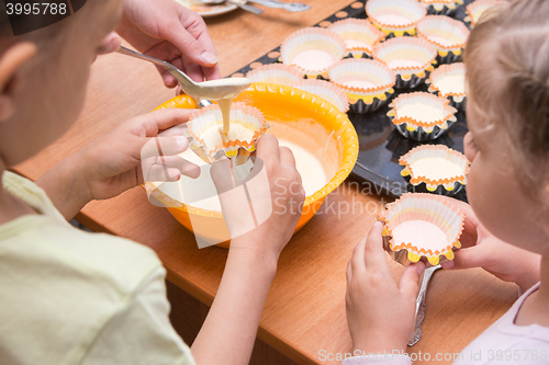 Image of Two girls helped mom to pour batter into the molds for cupcakes