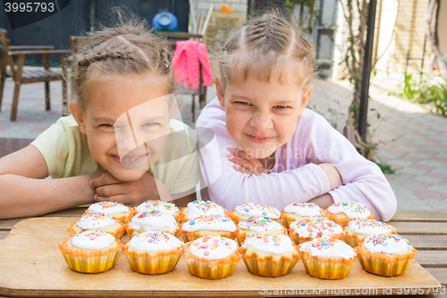 Image of Two girls pretending funny faces, sitting in front of easter cupcakes