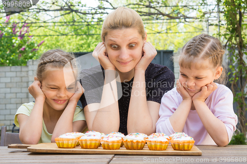 Image of Mother and two daughters with different funny emotion looking at easter cupcakes