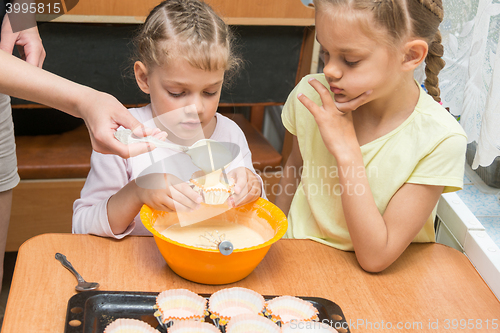 Image of Mom helps subsidiaries to pour batter into molds for baking cakes