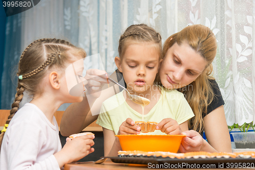 Image of Mother and two children baking pour the mass into molds preparing muffins for Easter