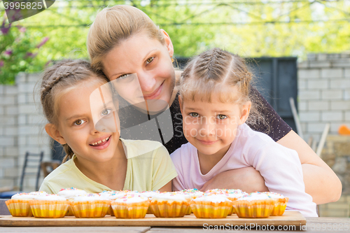Image of Mother hugging her daughters who cook delicious cupcakes