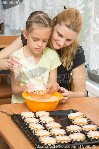 Image of Mother helps daughter to pour batter into the mold for cupcakes